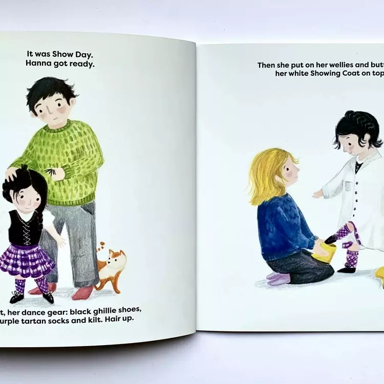 Thrown pages of illustrations from the highland cowgirl showtime, the first illustration shows Hanna having her hair pinned up by her dad. Hanna is dressed in a purple kilt, and the cat is by their legs, watching. The second illustration is of Hanna with